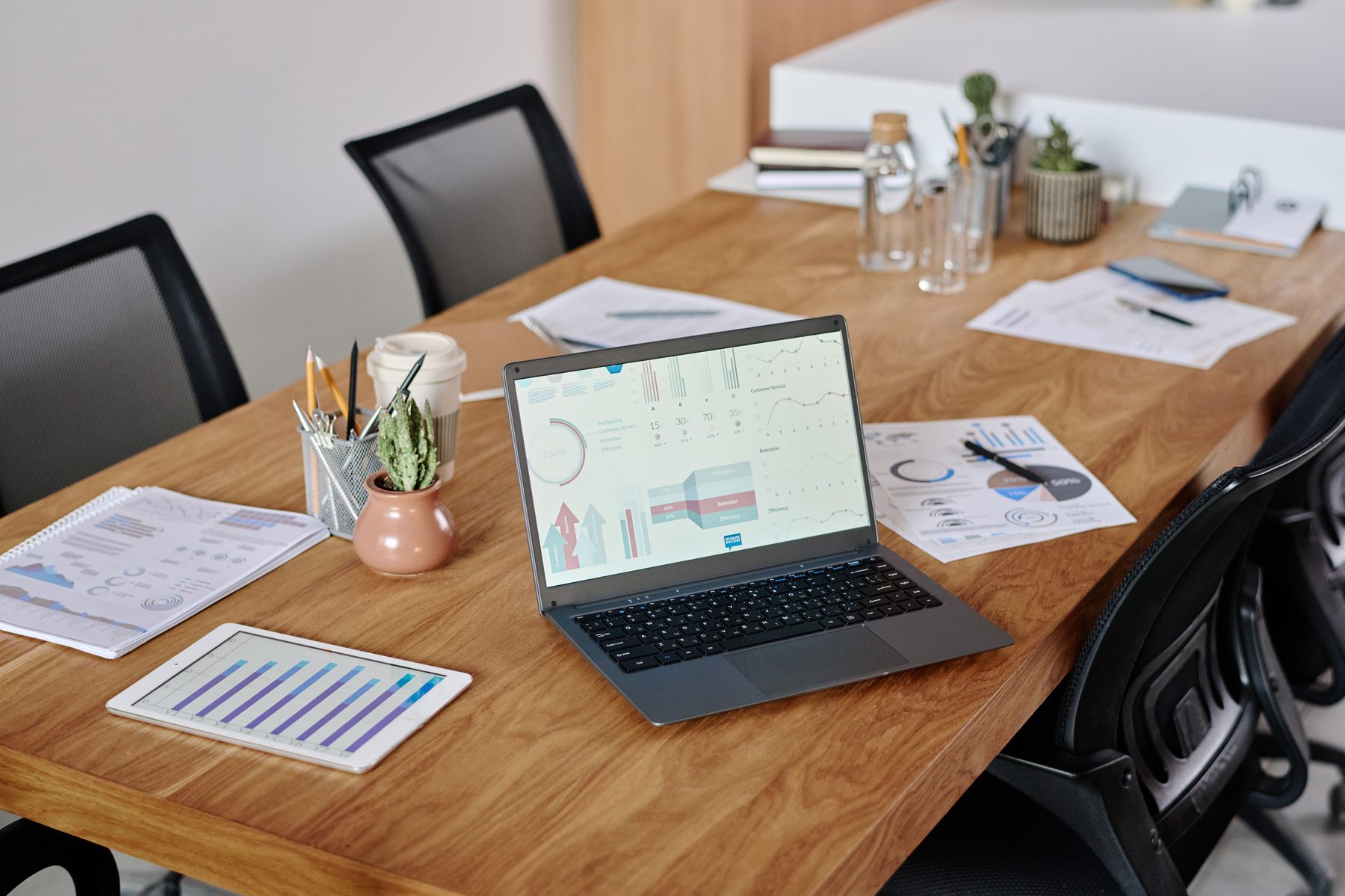 A workspace with a laptop showing analytics dashboards alongside printed reports and a tablet